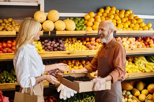 Happy mature woman in casual attire smiling at seller that helping her to choose fresh blackberries — Stock Photo