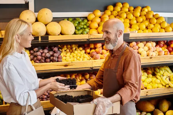 Bärtiger, fröhlicher Verkäufer, der seiner Kundin bei der Auswahl von Brombeeren hilft, einander lächelnd — Stockfoto