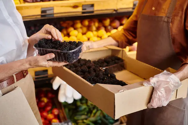 Cropped view of mature seller helping his customer to choose fresh blackberries at grocery store — Stock Photo
