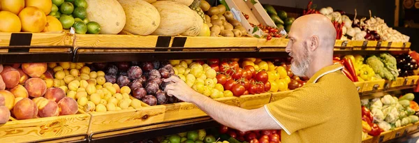 Reife Kundin in Freizeitkleidung mit Einkaufskorb mit frischen Pflaumen im Supermarkt, Banner — Stockfoto