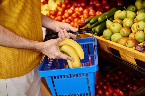 Vista recortada del cliente macho maduro poniendo plátanos frescos en la cesta de la compra en la tienda de comestibles - foto de stock