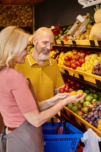 Сосредоточиться на радостный зрелый мужчина с корзиной получения помощи от продавщицы при выборе фруктов — стоковое фото