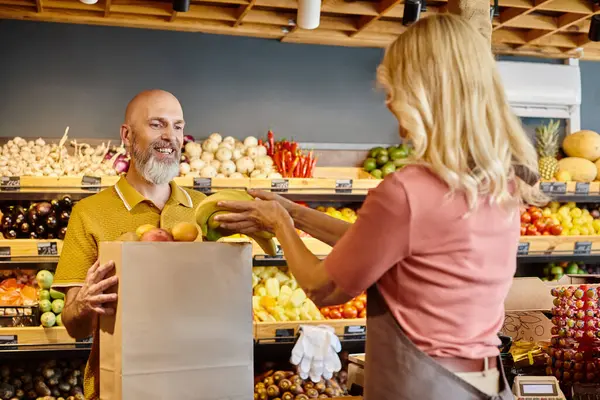 Concentrarsi sul cliente allegro sorridente accanto al venditore femminile offuscata mettendo banane fresche nel sacchetto di carta — Foto stock