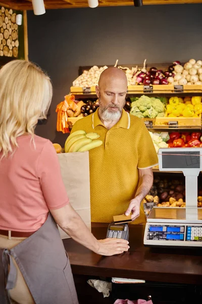 Vollbärtiger Kunde bezahlt mit Kreditkarte für Obst neben erwachsenem Verkäufer im Supermarkt — Stockfoto