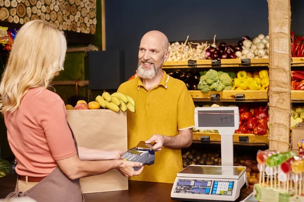 Fokus auf fröhliche Kunden, die mit dem Handy für frisches Obst bezahlen und verschwommene Verkäufer anlächeln — Stockfoto