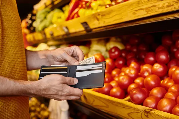 Abgeschnittene Ansicht eines reifen Käufers, der Geld aus seinem Portemonnaie in der Hand hält und bereit ist, im Lebensmittelgeschäft zu bezahlen — Stockfoto