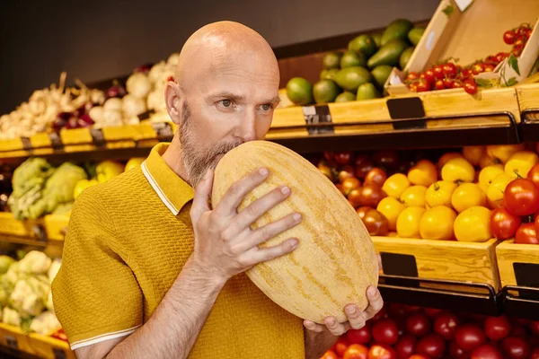 Gut aussehende konzentrierte reife männliche Kundin überprüft, ob Melone im Lebensmittelgeschäft frisch ist — Stockfoto