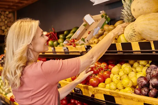 Зрілий веселий продавець посміхається під час роботи поруч з продуктовою кабінкою зі свіжими фруктами та овочами — стокове фото