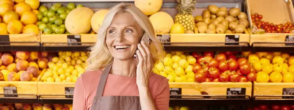 Feliz vendedor femenino sonriendo y hablando por teléfono con frutas y verduras en el telón de fondo, pancarta - foto de stock