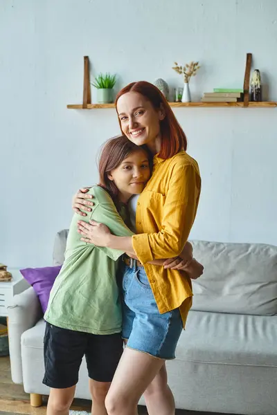 Cheerful woman with teen daughter embracing and looking at camera at home in cozy living room — Stock Photo