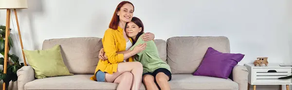 Радостная женщина с дочерью-подростком обнимается и смотрит в камеру на диване в гостиной, баннер — стоковое фото