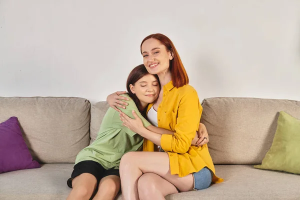 Cheerful woman with teenage daughter sitting and embracing on cozy couch in modern living room — Stock Photo