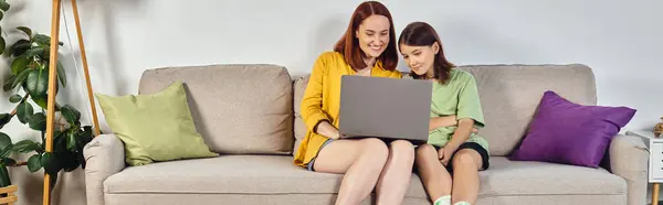 Щаслива жінка з дочкою-підлітком дивиться фільм на ноутбуці на дивані у вітальні, банер — стокове фото