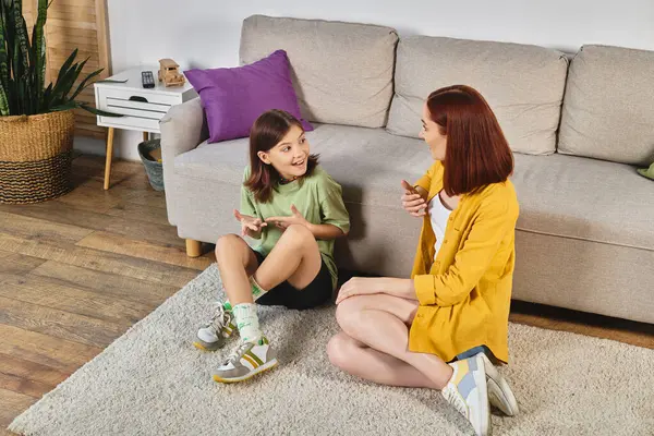 Excited teenage girl gesturing and talking with mother about sex education on floor at home — Stock Photo
