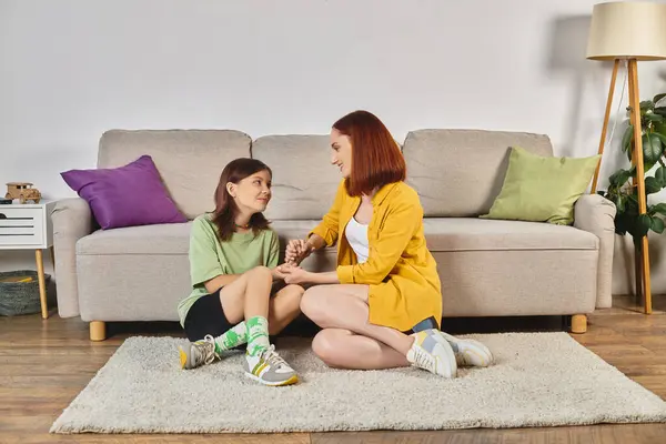 Smiling woman with teenage daughter holding hands and talking about sex education on floor at home — Stock Photo