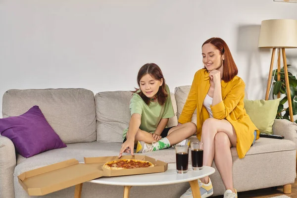 Mãe alegre e filha adolescente sentada no sofá perto de pizza e óculos com refrigerante na sala de estar — Fotografia de Stock