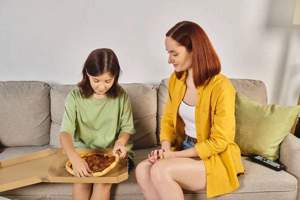 Preteen girl sitting on couch with delicious pizza near smiling mother on couch in living room — Stock Photo