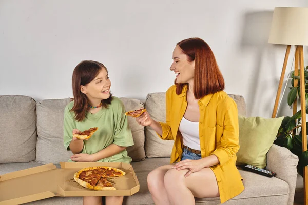 Cheerful mother and teenage daughter eating tasty pizza on cozy couch in living room, pizza time — Stock Photo