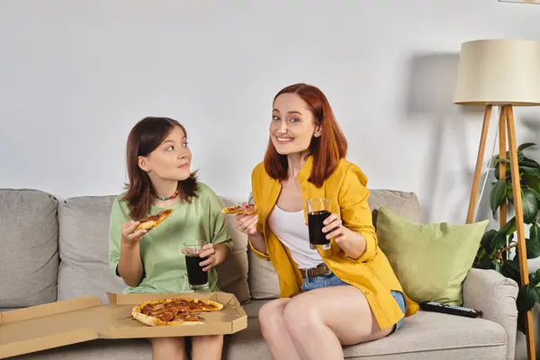 Cheerful mother and teenage daughter with pizza and soda on cozy couch in living room, pizza time — Stock Photo