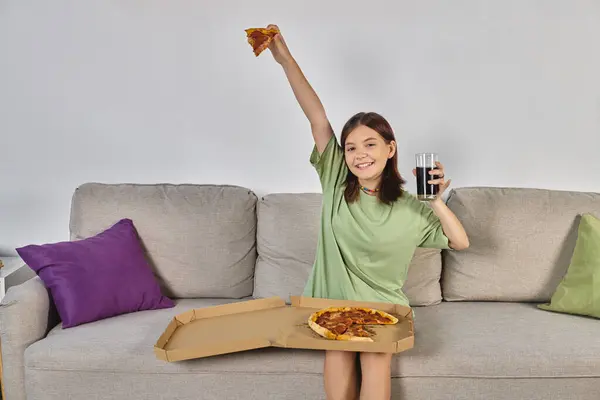 Animado adolescente sentada no sofá com pizza e copo de cola e olhando para a câmera, hora da refeição — Fotografia de Stock