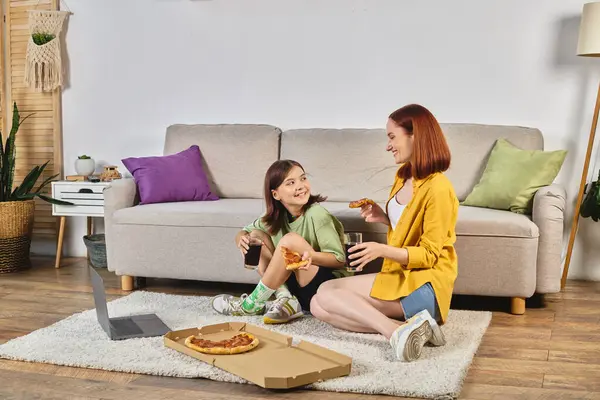 Happy mother and teen daughter with pizza and soda watching movie on laptop on floor in living room — Stock Photo