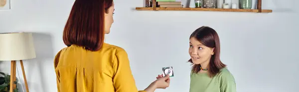 Madre mostrando condón a confusa hija adolescente en casa, educación sexual, pancarta horizontal - foto de stock