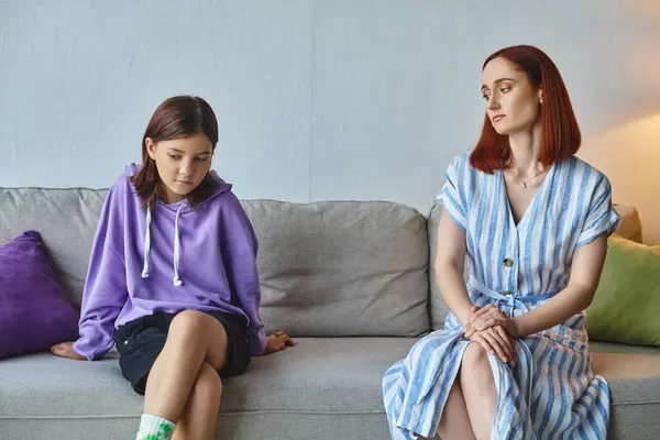 Thoughtful woman looking at frustrated teenage daughter on couch in living room, care and support — Stock Photo