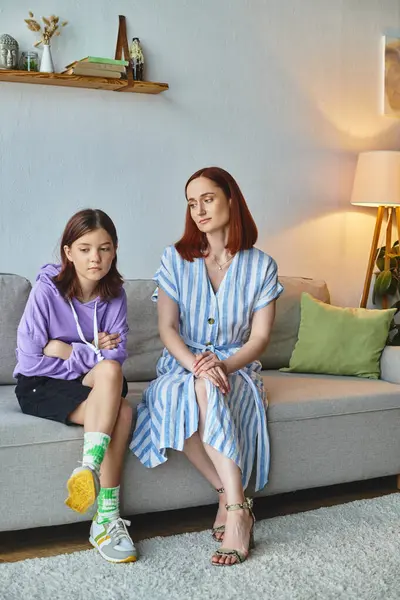 Thoughtful woman looking at frustrated teenage daughter on couch in living room, care and support — Stock Photo