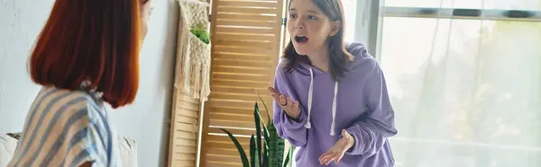 Роздратована дівчина-підліток кричить і свариться з матір'ю вдома у вітальні, банер — стокове фото