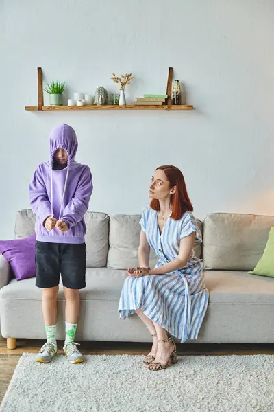 Worried and upset woman talking to offended daughter hiding in hood in living room, generation gap — Stock Photo