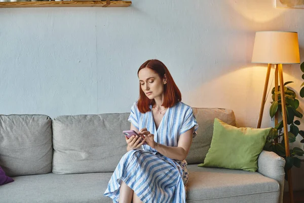 Messaggistica donna adulta sul telefono cellulare mentre seduto su un accogliente divano in soggiorno, vita domestica — Foto stock