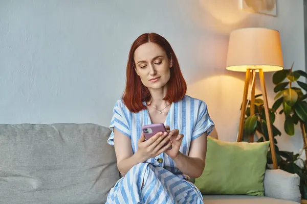 Stylish woman browsing internet on smartphone on cozy couch in modern living room, domestic life — Stock Photo