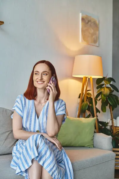 Happy stylish woman smiling and talking on smartphone on cozy couch in modern living room — Stock Photo