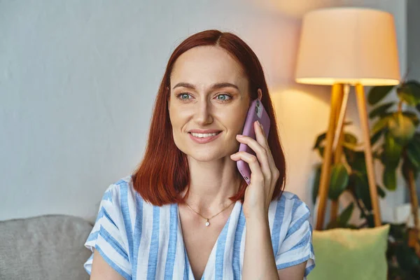 Happy stylish woman smiling and talking on smartphone in modern living room, domestic scene — Stock Photo