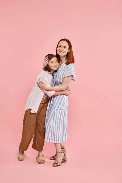 Повна довжина стильної і радісної жінки з дочкою-підлітком, що обіймається на рожевому тлі, щаслива сім'я — стокове фото