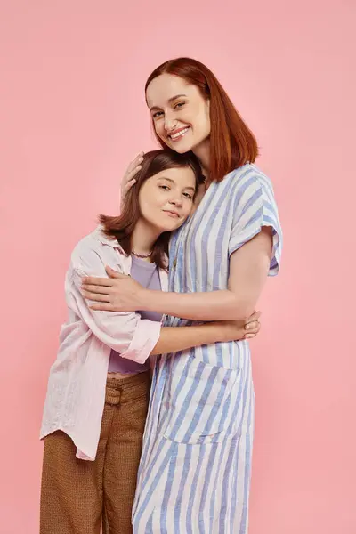 Mulher feliz com filha adolescente em trajes casuais elegantes abraçando e olhando para a câmera em rosa — Fotografia de Stock