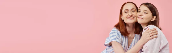 Joyful and trendy woman with teenage daughter embracing and looking at camera on pink, banner — Stock Photo