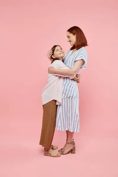 Full length of joyful woman with teenage daughter embracing and looking at each on pink backdrop — Stock Photo