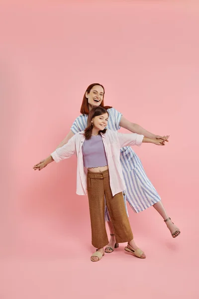 Веселая и стильная женщина, держась за руки дочери-подростка, позируя на розовом фоне — стоковое фото