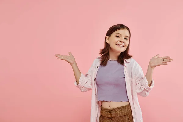 Щаслива дівчина-підліток в стильному повсякденному вбранні позує з відкритими руками і дивиться на камеру на рожевому — стокове фото