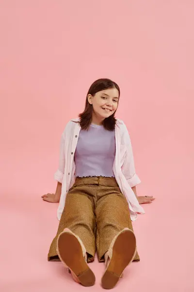 Comprimento total da menina adolescente alegre em trajes casuais na moda sentado e sorrindo para a câmera em rosa — Fotografia de Stock
