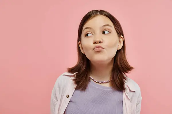 Positive and curious teenage girl in trendy clothes pouting lips and looking away on pink backdrop — Stock Photo