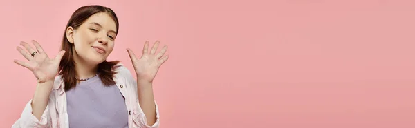 Adolescent gai fille en vêtements décontractés élégants agitant les mains et regardant la caméra sur rose, bannière — Photo de stock