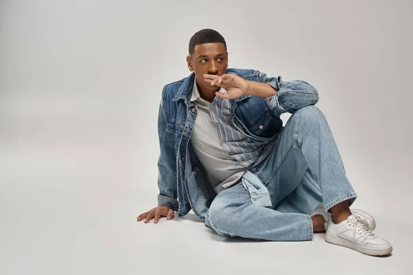 Good looking young african american man in trendy denim outfit sitting on floor, fashion concept — Stock Photo