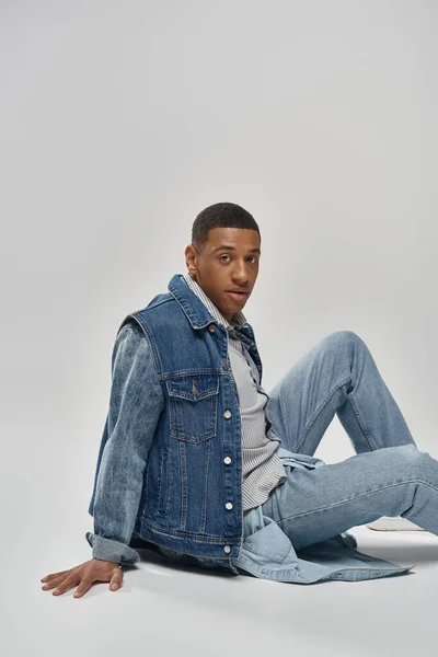 Bell'aspetto giovane uomo africano americano in abito di denim alla moda seduto sul pavimento, concetto di moda — Foto stock