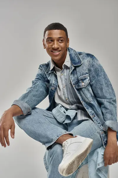 Good looking african american male model in denim outfit sitting on white cube, fashion concept — Stock Photo