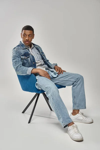 Bell'uomo afro-americano in elegante vestito di denim seduto sulla sedia blu, concetto di moda — Foto stock