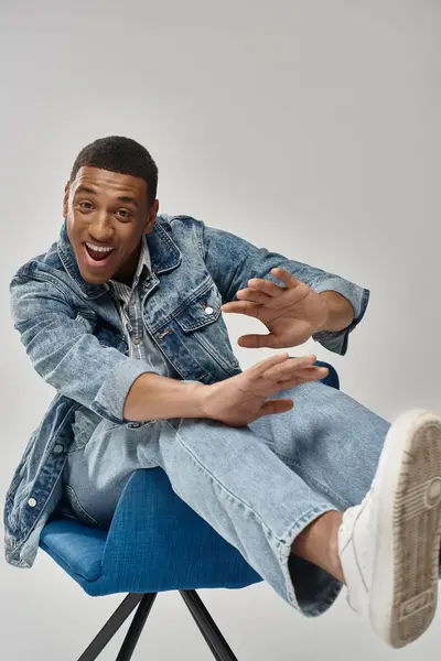 Handsome african american man in stylish denim outfit sitting on blue chair, fashion concept — Stock Photo
