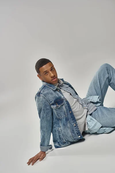 Good looking young african american man in trendy denim outfit sitting on floor, fashion concept — Stock Photo