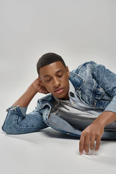 Good looking young african american man in trendy denim outfit lying on floor, fashion concept — Stock Photo